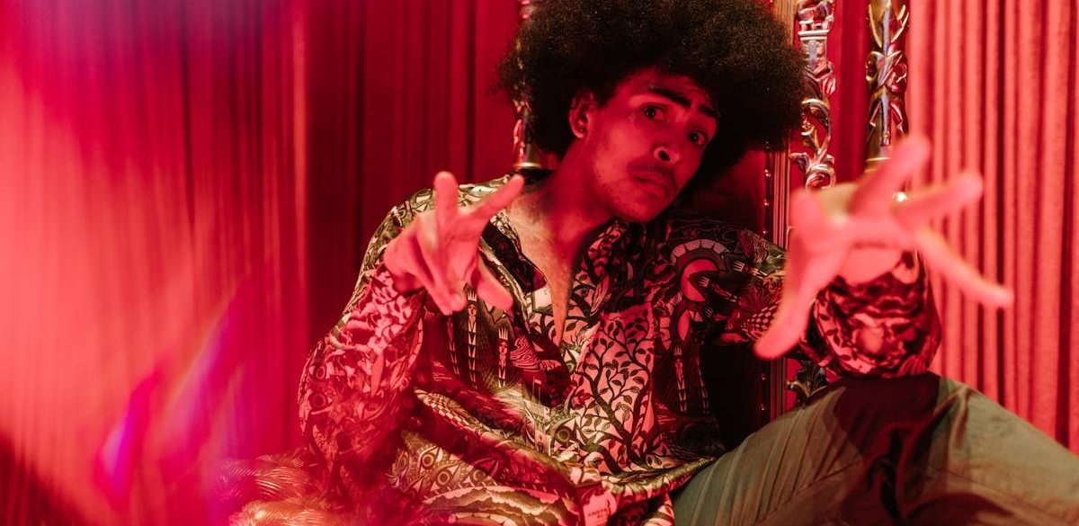 Man in vibrant outfit and afro hairstyle posing in a creative indoor setting.