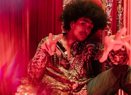 Man in vibrant outfit and afro hairstyle posing in a creative indoor setting.
