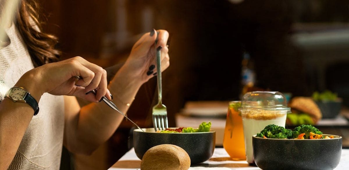A woman dining on a fresh salad with vegetables and a drink indoors.