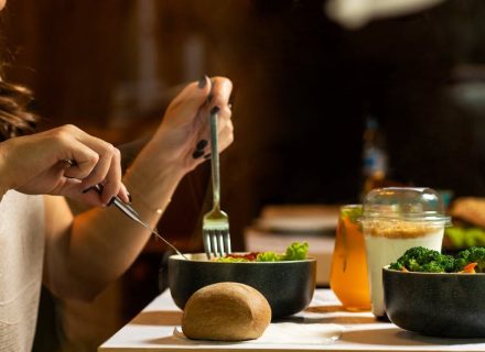 A woman dining on a fresh salad with vegetables and a drink indoors.