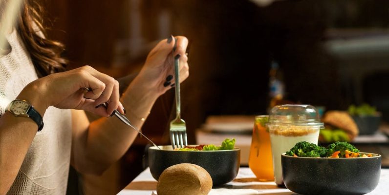 A woman dining on a fresh salad with vegetables and a drink indoors.