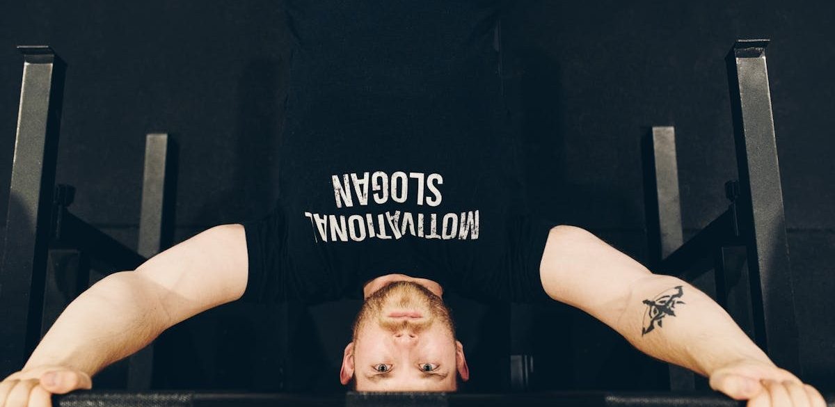 Bearded sportsman in t shirt with inscription exercising with weight while looking at camera