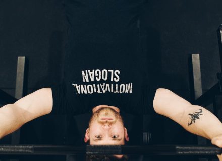 Bearded sportsman in t shirt with inscription exercising with weight while looking at camera