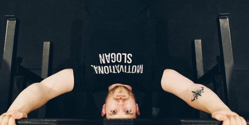 Bearded sportsman in t shirt with inscription exercising with weight while looking at camera